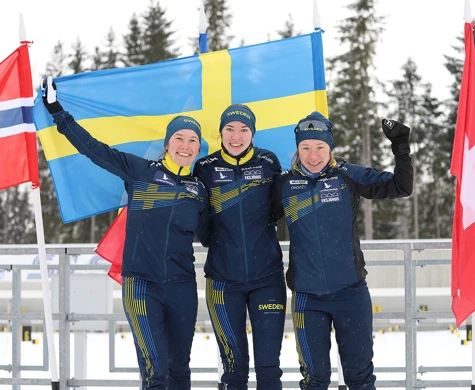 Guldtrion Evelina Wickbom, Elin Schagerström och Lisa Larsen med stora leenden framför den svenska flaggan.