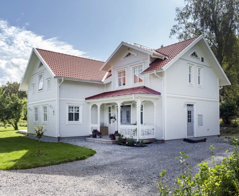 En vit trävilla, tillverkad av Eksjöhus, belägen i en solig trädgård.
