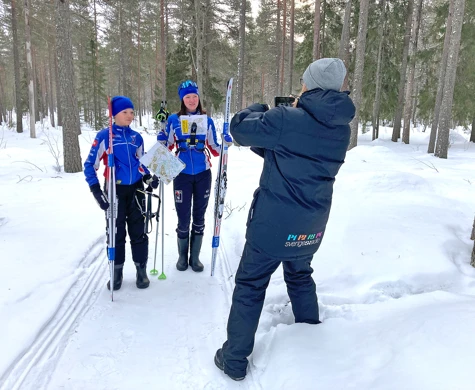 OK Renen-ungdomarna Iris och Ellen Bergkvist står på ett skoterspår med skidorienteringsutrustning tillsammans med reportern Tova Nilsson från SR Norrbotten.