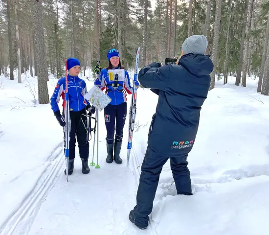 OK Renen-ungdomarna Iris och Ellen Bergkvist står på ett skoterspår med skidorienteringsutrustning tillsammans med reportern Tova Nilsson från SR Norrbotten.