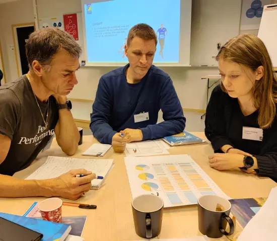 Tre deltagare på Junior- och seniortränarutbildningen sitter vid ett bord och funderar kring en övningsuppgift